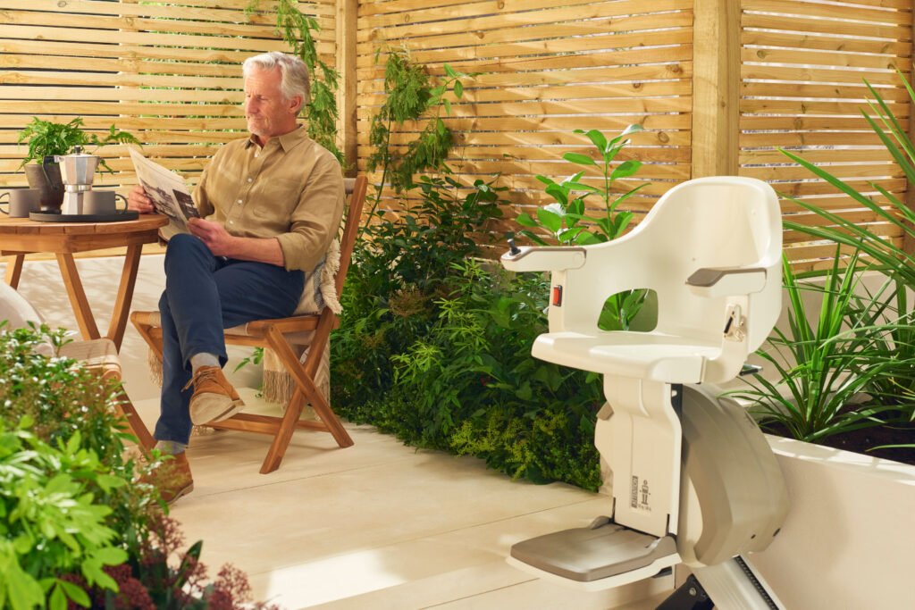 An elderly man relaxing in a garden with an Access Straight Outdoor Stairlift installed on a low wall.
