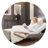 A person comfortably sitting up in an adjustable bed, with the bed frame slightly raised at the head end.