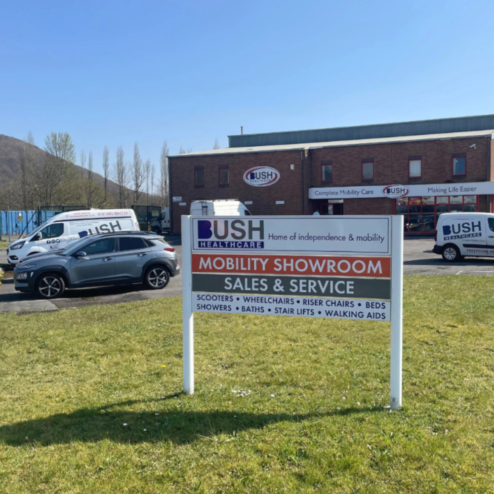 An outdoor sign for Bush Healthcare's Aberdare Mobility Showroom, listing various products like scooters, wheelchairs, beds, and stairlifts.