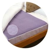 A close-up of a bed with a lilac incontinence mattress protector or pad visible.