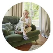 A person comfortably seated on a green armchair, wearing patterned slippers from Cosyfeet.