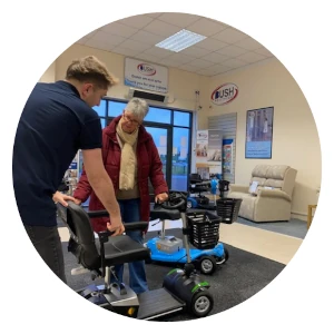A Bush Healthcare staff member demonstrating a mobility scooter to an elderly female customer inside a showroom.