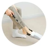 A person using a long-handled sock aid to put on a white sock, demonstrating a daily living aid.