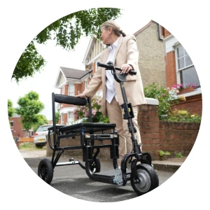 A person using a compact, folded eFoldi Lite mobility scooter in a modern urban outdoor setting, with houses and greenery in the background, highlighting its portability.