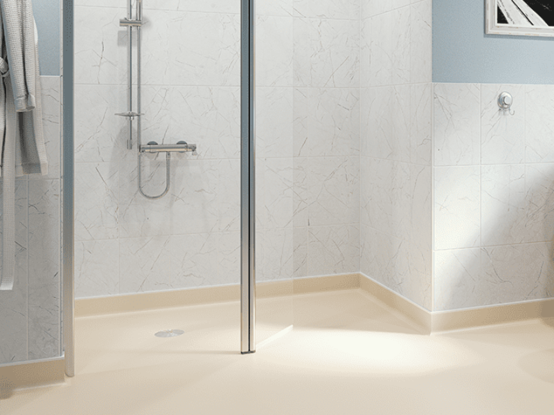 A section of an accessible bathroom with non-slip flooring, a shower with a low-level tray, and grab rails on a tiled wall.