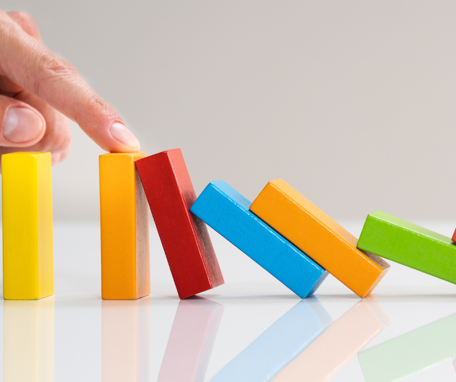 Multicoloured dominos falling over with a human finger preventing them from continuing to fall.