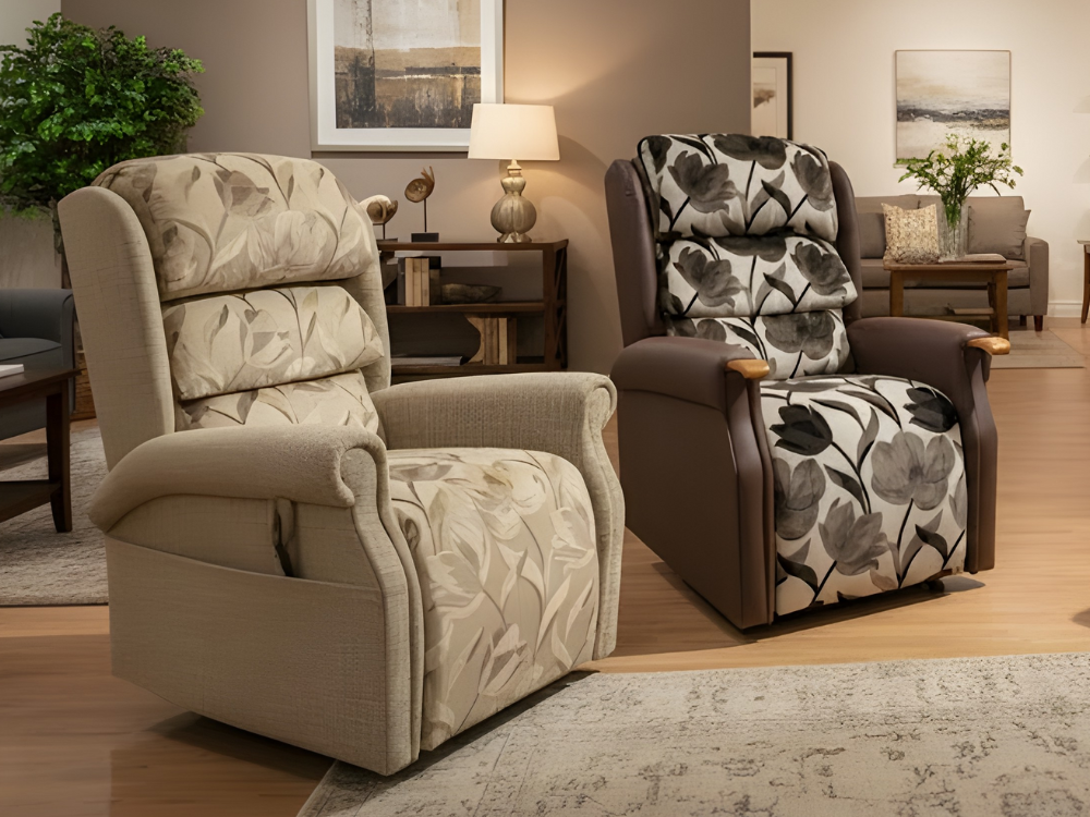 Two riser recliner chairs from the Castle Range in a living room showroom setting, one featuring a bold, patterned floral fabric and the other a floral beige fabric.