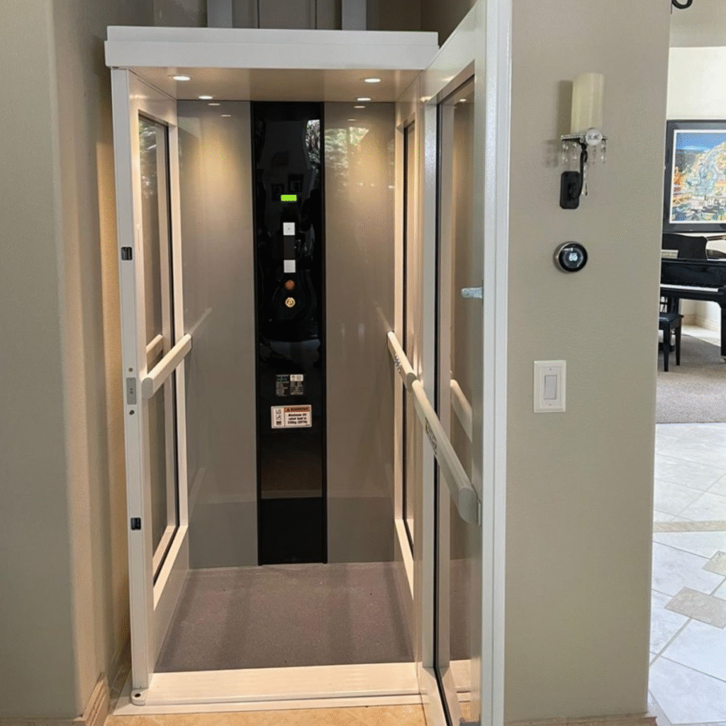 White and glass Pollock indoor vertical lift installed discreetly within an interior wall opening of a modern home with wood flooring.