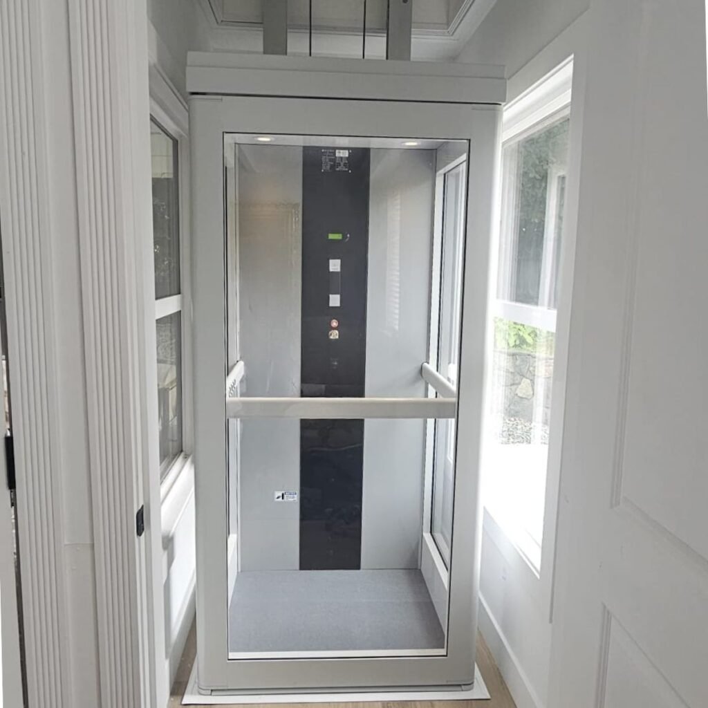 Interior view of the white and glass Pollock indoor vertical lift cabin, showing the control panel and the surrounding living space.