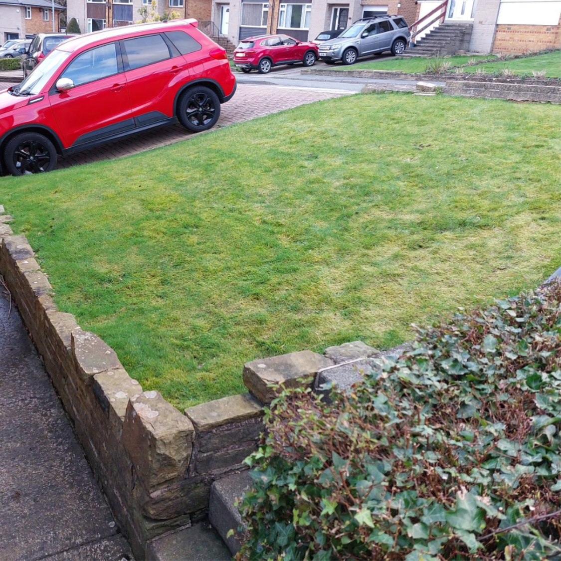 Grassy, hilly front garden and entry steps with a low stone wall, showing the outdoor space before the Pollock Steplift is installed.