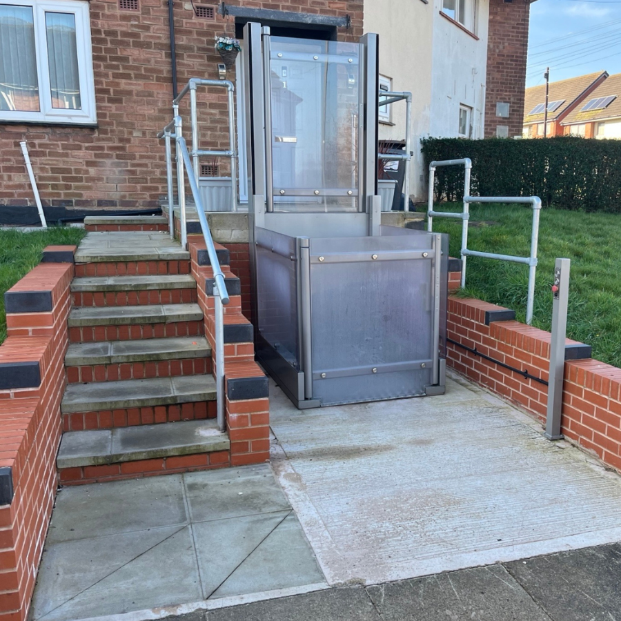 Silver Pollock Steplift Outdoor vertical platform lift installed on a concrete landing next to brick steps, demonstrating a 2 metre rise installation outside a residential home.
