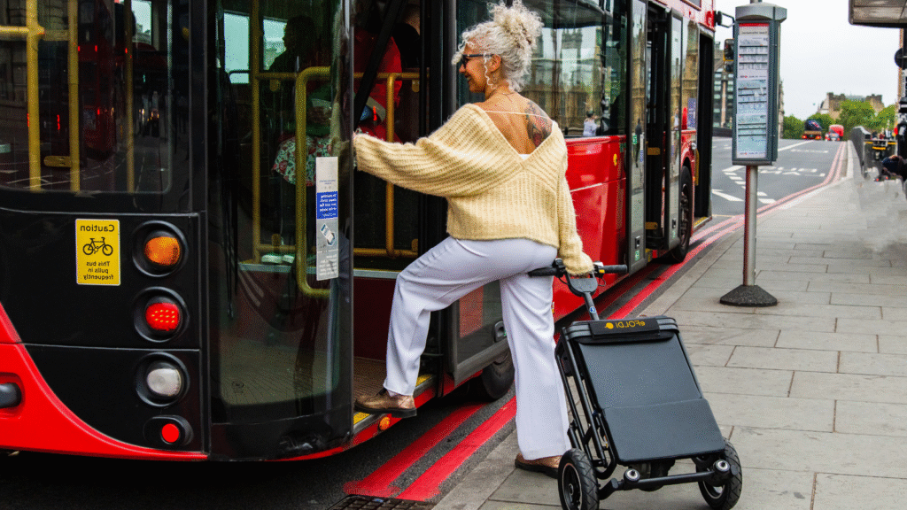 Woman stepping onto a red city bus while easily wheeling the black eFoldi mobility scooter, which is compactly folded into a luggage cart.