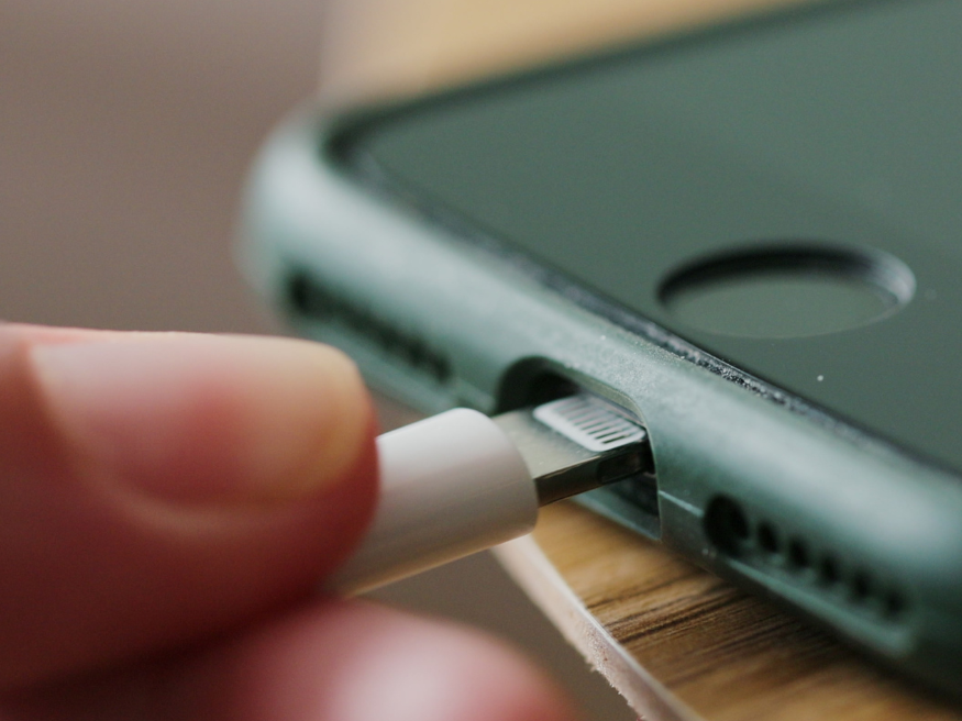 Close-up of a finger plugging a USB cord into the charging port on the side of a mobile phone, representing the ability to add a USB charger to a riser recliner chair.